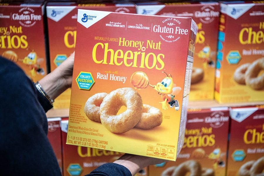 A girl holds up a box of Cheerios