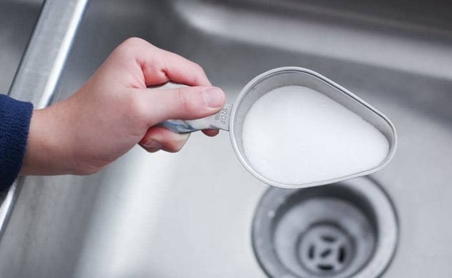 A scoop of salt is held over a sink